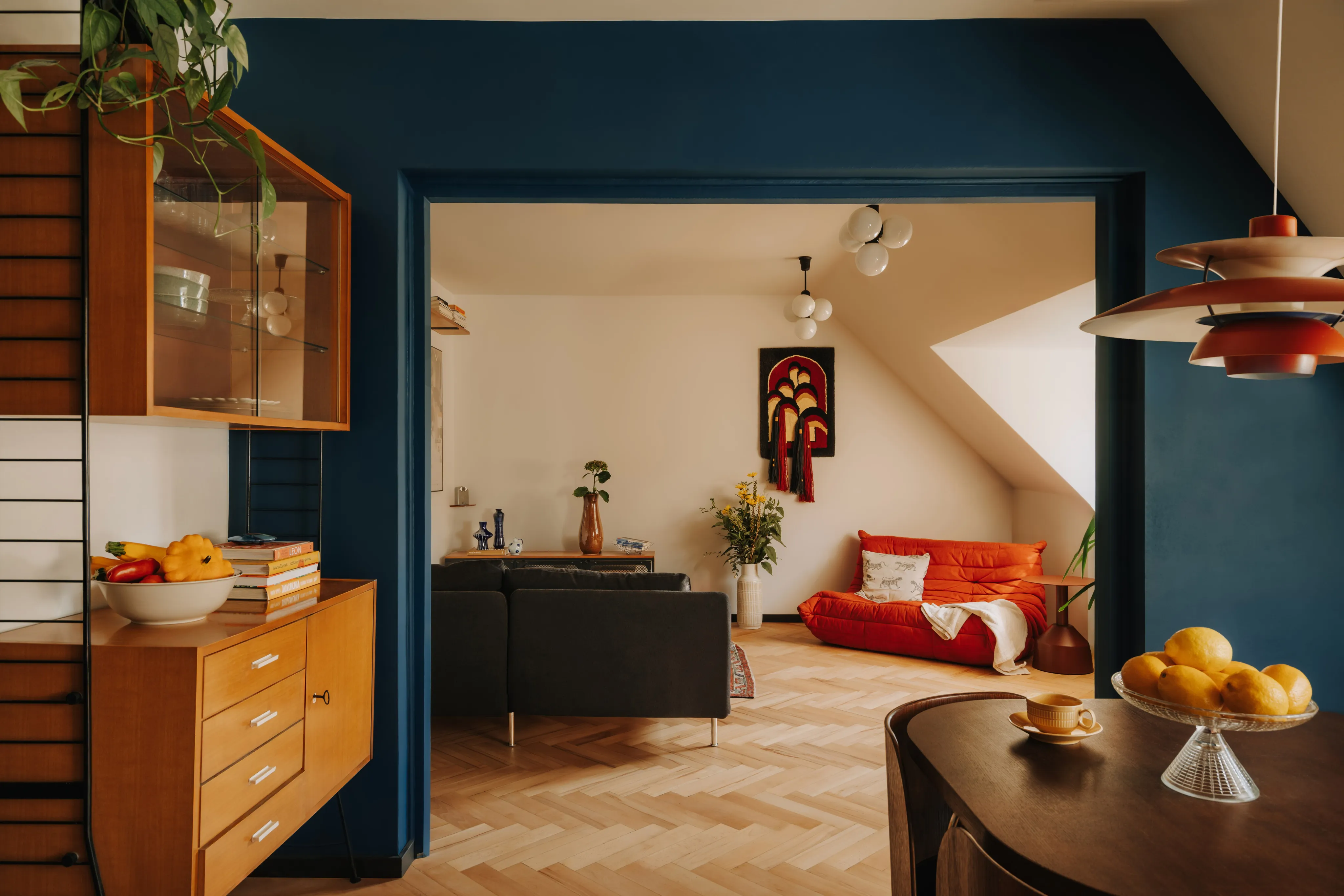 Salon z granatową ścianą, pomarańczową sofą i drewnianymi meblami vintage w projekcie Kamiko