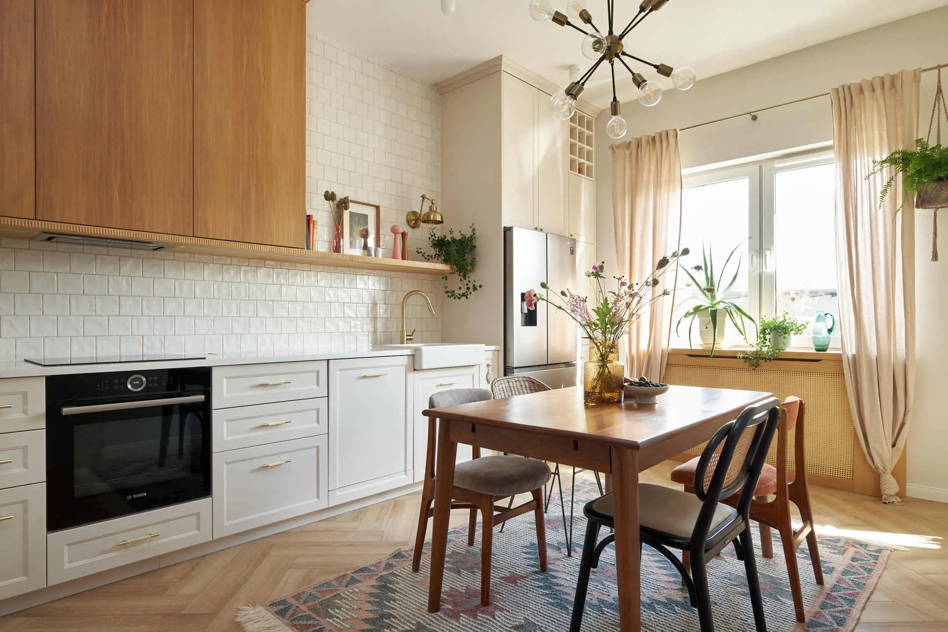 Nowoczesna kuchnia z jadalnią: białe szafki, drewniane blaty, kaflowy backsplash, drewniany stół z krzesłami w stylu mid-century oraz bujne rośliny przy panoramicznym oknie.