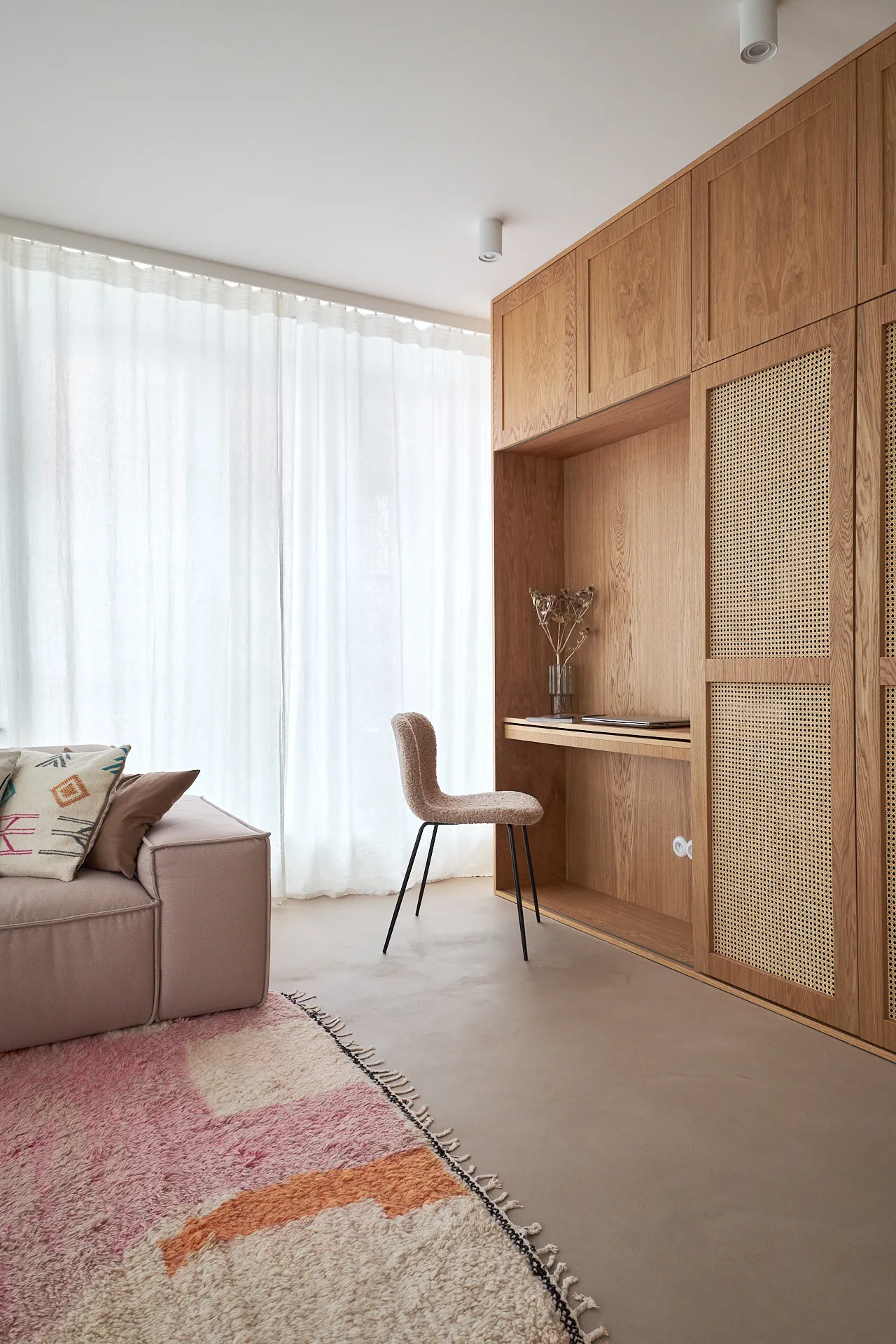 Nowoczesna aranżacja salonu z drewnianą ścianą z otworami w stylu boho, miękką sofą w beżu, wygodnym krzesłem i geometrycznym dywanem w odcieniach różu i złota.